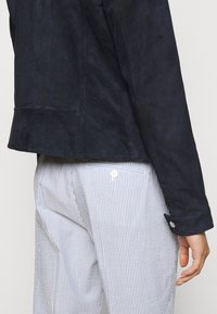 Námořnická sametová bunda s texturovaným povrchem, která má přiléhavý střih a zapínací manžety, v kombinaci s modro-bílými pruhovanými kalhotami.