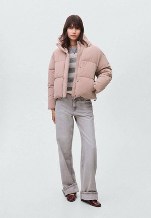 Doudoune beige clair, avec une coupe courte, un motif matelassé et des fermetures à pression. Associée à un jean gris évasé et des chaussures foncées.