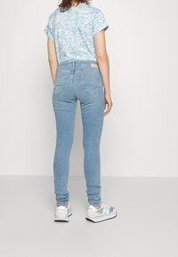 Camiseta de color azul claro con estampado, jeans ajustados de color azul claro y zapatillas blancas con acentos azules. Vista desde la espalda, mostrando el ajuste del atuendo.