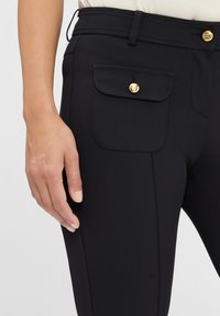 Schwarze maßgeschneiderte Hose aus strukturiertem Stoff, mit einer Vordertasche und einem goldenen Knopf, flachen Vorderteil und sichtbaren Nähten.