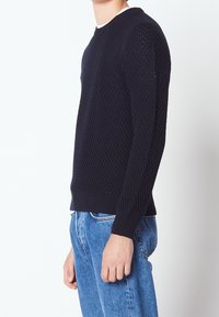 Pull en maille bleu marine avec un motif texturé, col rond et poignets côtelés. Assorti à un jean en denim bleu clair.