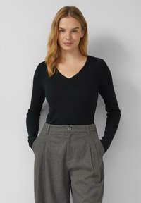Czarny prążkowany top z długim rękawem i dekoltem w kształcie litery V, zestawiony z szarą plisowaną spódnicą z zapięciem na guziki i bocznymi kieszeniami.