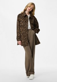 Chaqueta de estampado de leopardo con cuello de solapa, botones, mangas largas y bolsillos laterales, combinada con pantalones de pierna ancha beige y zapatillas blancas.