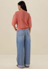 Gehaakte koraaltruik met korte mouwen, met een kantdesign. Gepaarde met lichtblauwe wijde spijkerbroek met opgerolde manchetten. Simpel en casual.