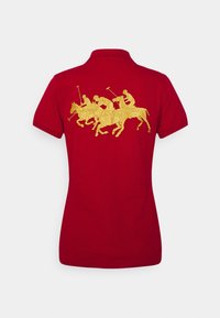 Camisa polo roja con un diseño dorado bordado de cuatro jugadores de polo a caballo. Con mangas cortas y detalle de cuello clásico.