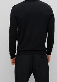 Schwarzer Strickpullover mit langen Ärmeln, Rundhalsausschnitt sowie gerippten Bündchen und Saum. Glatte Textur, figurbetonte Silhouette und reduzierte Designdetails.