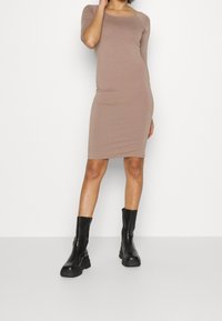 Brązowa dopasowana sukienka bodycon z krótkim rękawem, wykonana z gładkiego materiału. W zestawie z czarnymi botkami za kostkę o grubych podeszwach. Prosty, elegancki design.