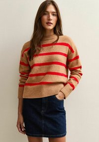 Maglione lavorato a maglia beige con righe rosse, collo rotondo, polsini e orlo a coste. Abbinato a una mini gonna in denim scuro con tasche frontali.