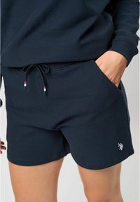 Námořnické modré šortky vyrobené z texturované látky, s širším stahováním v pase v červené a bílé barvě a bočními kapsami. Malé logo na lemu.