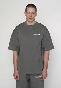 Graues übergroßes T-Shirt aus Baumwolle, mit kurzen Ärmeln und Rundhalsausschnitt. "MULTIPLY"-Logo in Weiß auf der linken Brustseite.
