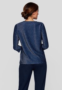 Navyblaues langärmeliges Oberteil aus schimmerndem Stoff, mit entspannter Passform und rundem Ausschnitt, einer glatten, leicht strukturierten Oberfläche.