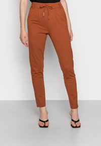 Kalhoty v měděné barvě, vyrobené z hladké tkaniny. Jsou slim-fit s elastickým pasem se šňůrkou a dvěma předními kapsami, doplněné černými sandály.