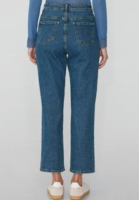 Džínové kalhoty s vysokým pasem a širokými nohavicemi, modré, s pěti kapsami, s hrubými lemy a mírně vybledlou texturou. V kombinaci s bílými teniskami.