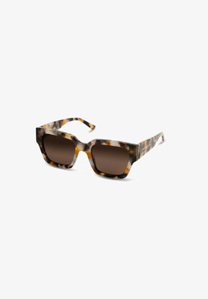 Lunettes de soleil avec une monture écaille de tortue épaisse et des verres marron, présentant une forme hexagonale et des branches élégantes avec un détail de marque subtil.