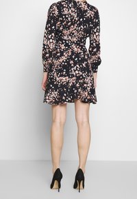 Svart blommig klänning med figursydd byst, långa ärmar och en utsvängd kjol. Rosa och vita blommönster över hela klänningen. Kombinerad med svarta klackskor.