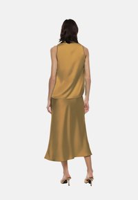 Abito senza maniche in seta di colore senape, che scende fino a metà polpaccio con orlo dritto, texture liscia e vestibilità comoda. Design minimalista.