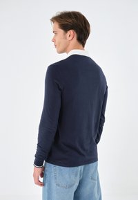 Marineblaues Langarm-Polohemd mit weißem Kragen und Bündchen; der Stoff wirkt weich und strukturiert und weist ein einfaches Design ohne Muster auf.