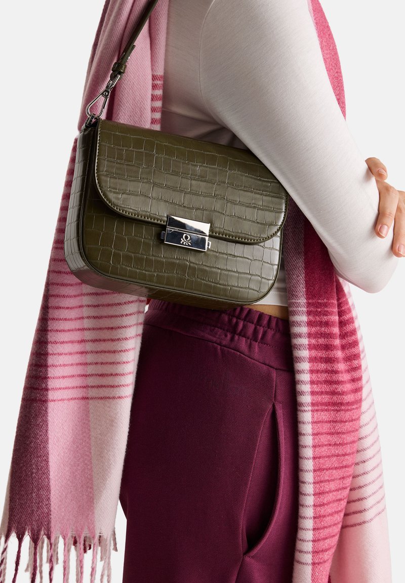 Torebka w oliwkowym kolorze z wzorem krokodyla, z srebrnym zapięciem, noszona obok różowo-prążkowanego szalika, założonego na jasną bluzkę i burgundowe spodnie.