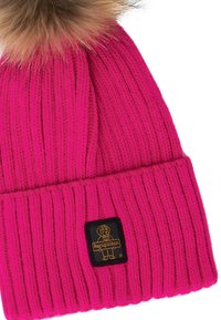 Cappello invernale lavorato a maglia di un vivace rosa con risvolto, un'etichetta nera con un logo di un cane dei cartoni animati e un pompon marrone soffice in cima.