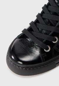 Fekete lakk bőr sneaker texturált felülettel, lekerekített orral, fekete fűzővel, ezüst fűzőlyukakkal és gumitalppal, amelyet gyémántmintázat díszít.