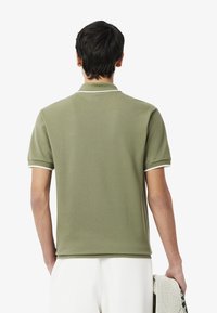 Polo shirt verde oliva con maniche corte, colletto bianco e rifiniture sulle maniche, realizzato in un tessuto testurizzato, presentato con una posa informale.