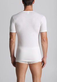 Camicia bianca a maniche corte realizzata in un tessuto morbido, design aderente, texture liscia, con scollo rotondo e dettagli di cucitura leggermente visibili.