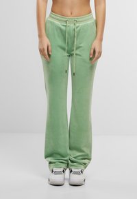 Grønne fløyels joggebukser med snor i midjen, vide ben og en glatt tekstur. Kombinert med hvite og svarte sneakers.