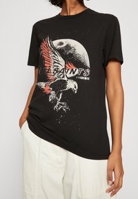 Svart bomull t-shirt med ett grafiskt tryck av en örn med röda accenter och en månbakgrund, rundad hals, korta ärmar.