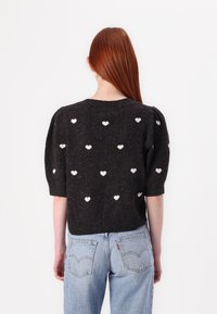 Maglione lavorato a maglia di un grigio scuro con maniche a sbuffo corte, che presenta motivo a cuori bianchi sparsi su tutta la superficie. Collo e orlo a coste.