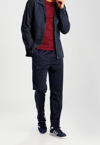 Chaqueta de cremallera navy sobre una camiseta burdeos, combinada con pantalones navy y zapatillas oscuras con rayas blancas. Un atuendo simple y casual.