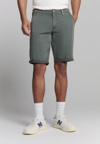 Grijze katoenen shorts met opgerolde zoom, voorzien van zijzakken en een knoopsluiting. Gecombineerd met witte sokken en schoenen met blauwe accenten.