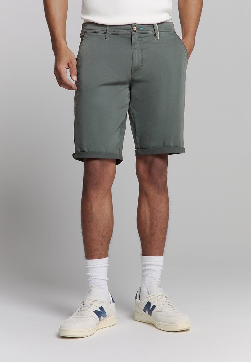 Grijze katoenen shorts met opgerolde zoom, voorzien van zijzakken en een knoopsluiting. Gecombineerd met witte sokken en schoenen met blauwe accenten.