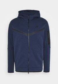 Nike navy hooded jacket with a zip front, featuring black accent stripes and a zip pocket on the left arm. Made from smooth, textured fabric.