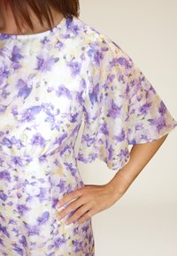 Blomstrete kjole med lilla og gule mønstre på et gjennomsiktig, lett stoff. Korte bell-ermer med løs passform og rund halsutringning.
