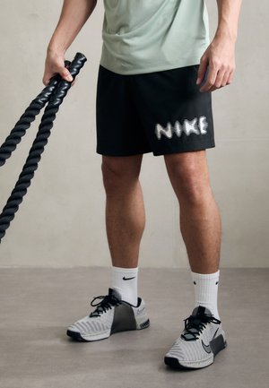 Črne športne kratke hlače z belim logotipom "NIKE", sivi in črni usnjeni čevlji ter bele nogavice do gležnjev. Model drži črne vajarske vrvi.