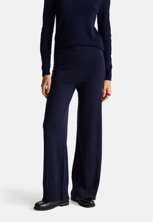 Pantalons larges bleu marine en tissu tricoté doux, dotés de poignets côtelés et d'une texture lisse. Associés à un haut à manches longues assorti.