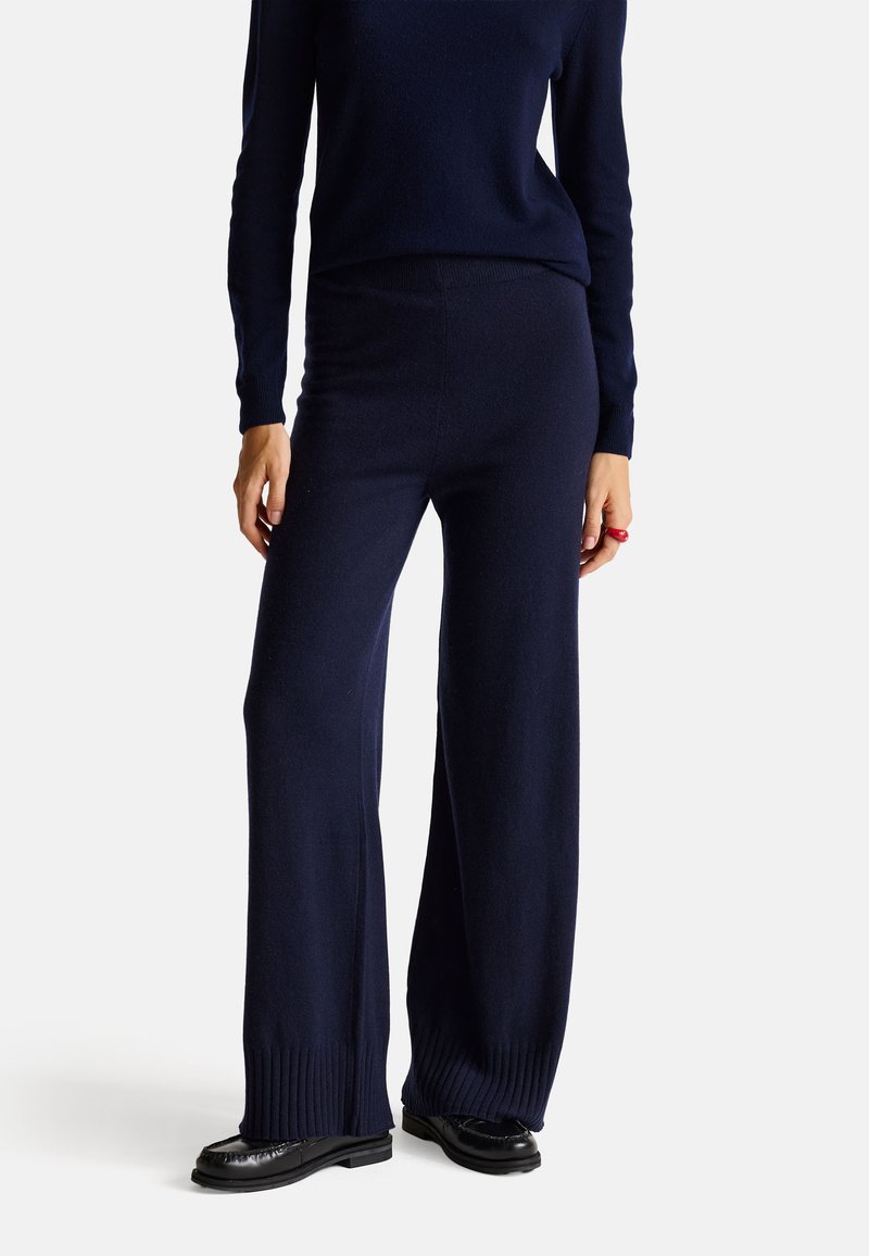 Pantaloni a gamba larga color navy realizzati in morbido tessuto a maglia, con polsini a coste e una texture liscia. Abbinati a un top a maniche lunghe coordinato.