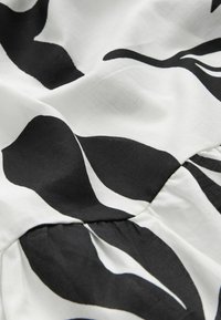 Tissu à motifs noir et blanc avec des formes de feuilles abstraites, texture lisse et détail froncé au niveau de la couture. Matériau léger et respirant.