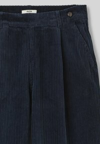 Pantalons en velours côtelé bleu marine avec des rayures verticales, fermeture à bouton et poches latérales, d'une coupe relaxée. Le tissu a une texture douce.
