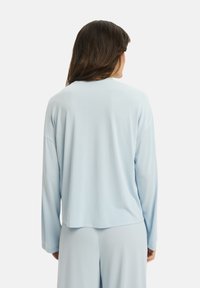 Jasnoniebieska bluzka z długim rękawem, wykonana z miękkiego materiału, o luźnym kroju, okrągłym dekolcie i lekko zaokrąglonym dole. Brak widocznych wzorów lub akcentów.