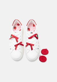 Baskets blanches avec des accents rouges, des fraises brodées et des lacets en ruban rouge. Comprend des lacets rouges supplémentaires. L'intérieur présente un motif de fraises.