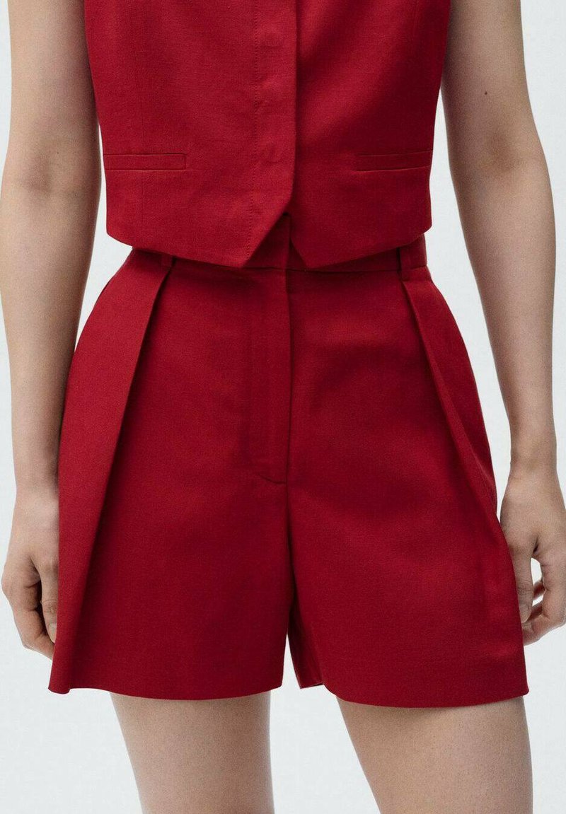 Red tailored shorts made of fabric with a smooth texture; feature pleats, side pockets, and a fitted waistband.