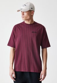 Bordo majica s kratkim rukavima s vertikalnim mornarskim prugama i izvezenim logom "New Era" na prsima. Lagana, prozračna tkanina.