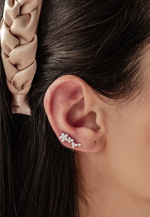 Silver ear cuff with multiple clear crystal accents, shaped like blossoms, attached to the ear lobe. Hair styled in a braid.