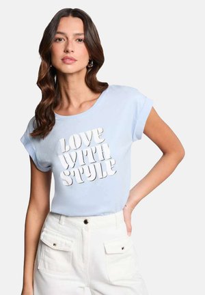 T-shirt bleu clair à manches courtes avec le texte "LOVE WITH STYLE" en blanc, associé à un pantalon blanc taille haute avec poches à rabat.
