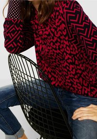 Långärmad topp med ett röd- och svart djurmönster på kroppen, samt ett mönstrat kontrast på ärmarna; kombinerad med denimjeans.