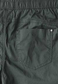 Donkergroene shorts met een gestructureerde oppervlakte, voorzien van een elastische tailleband en een patchzak met een metalen knoopdetail.