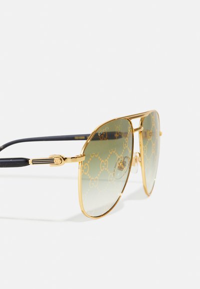 Occhiali da sole aviator dorati con lenti verdi sfumate, caratterizzati da un motivo GG intrecciato, con accenti neri sulle tempie e una montatura in metallo lucido.