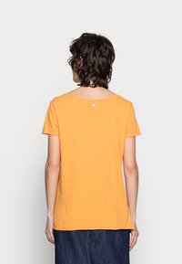 Kurzes, orangefarbenes T-Shirt aus weichem Stoff, mit weitem Ausschnitt und einem kleinen Akzentdetail auf der Rückseite.