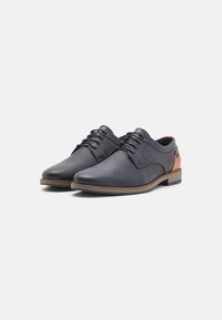 Pantofi din piele neagră cu o suprafață texturată, accente maro și design cu șireturi. Prezintă o talpă rezistentă și o formă a vârfului rotunjită.